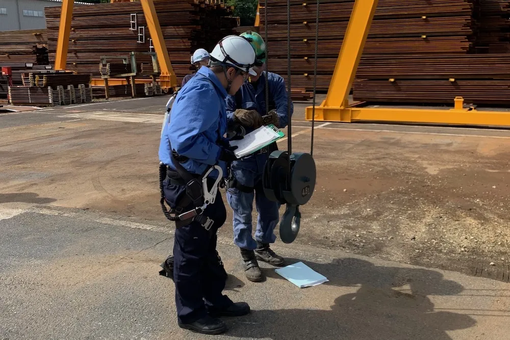 「2T」と書かれた重量物の前で計測作業を行う作業員