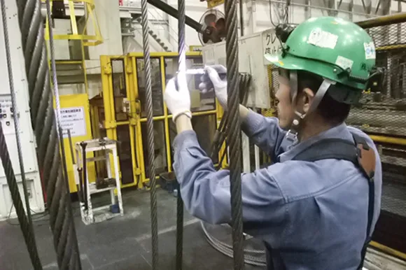 ワイヤーロープをライトで照らして点検する作業員
