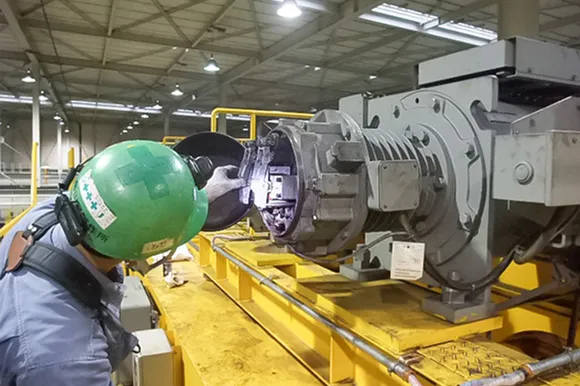 工場内で機械のギア部分をライトで照らして確認