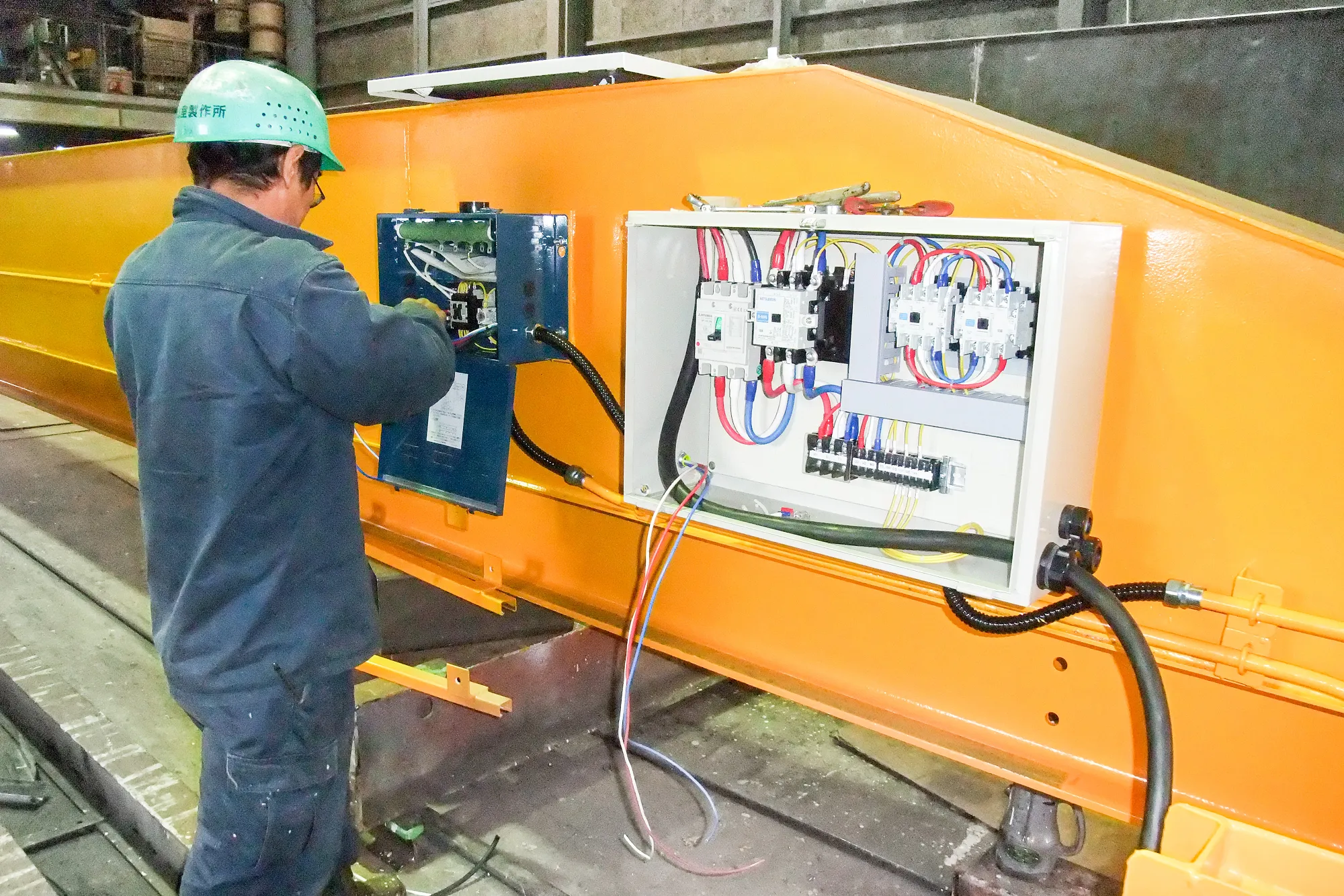 オレンジ色の大型機械に制御装置を取り付け中の様子
