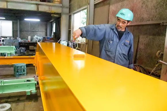 作業服を着たスタッフが部品に塗料を塗っている場面